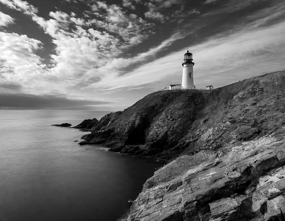 Medium size lighthouse on a cliff, blue sky, heavy clouds